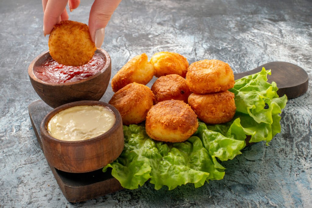 bottom-view-fried-cheese-balls-sauce-bowls-lettuce-cutting-board-cheese-ball-female-hand