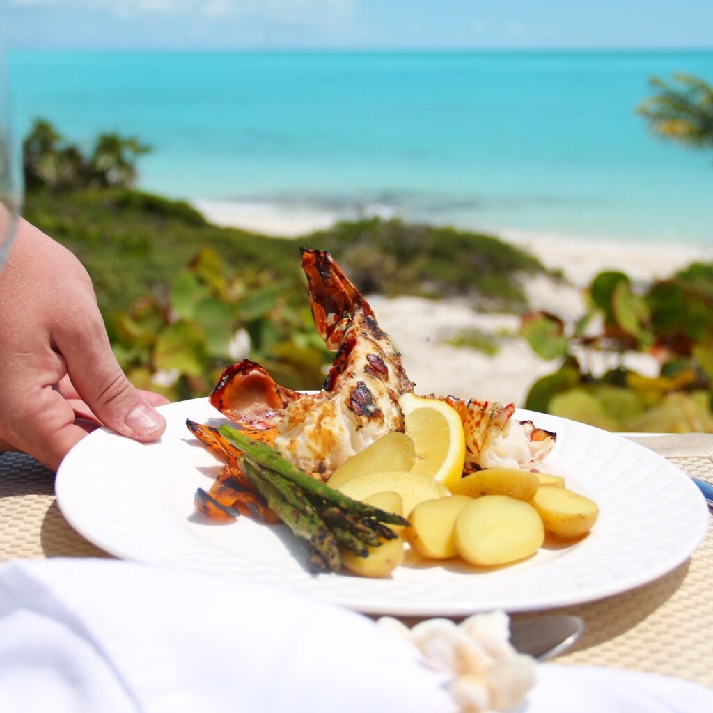 cropped-hand-person-holding-lobster-plate-by-beach