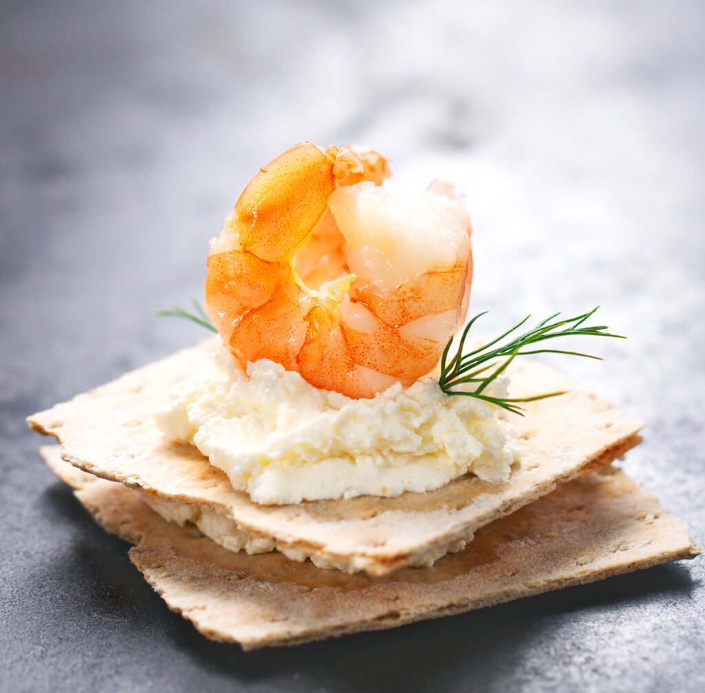 Appetizer canape with shrimp, cheese and dill on a small loaf of bread, closeup