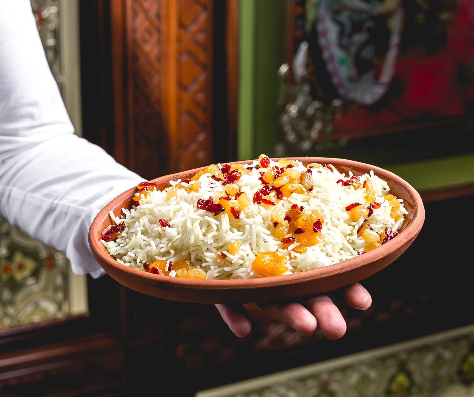 side view a man holds a plate with boiled rice with raisins and barberries