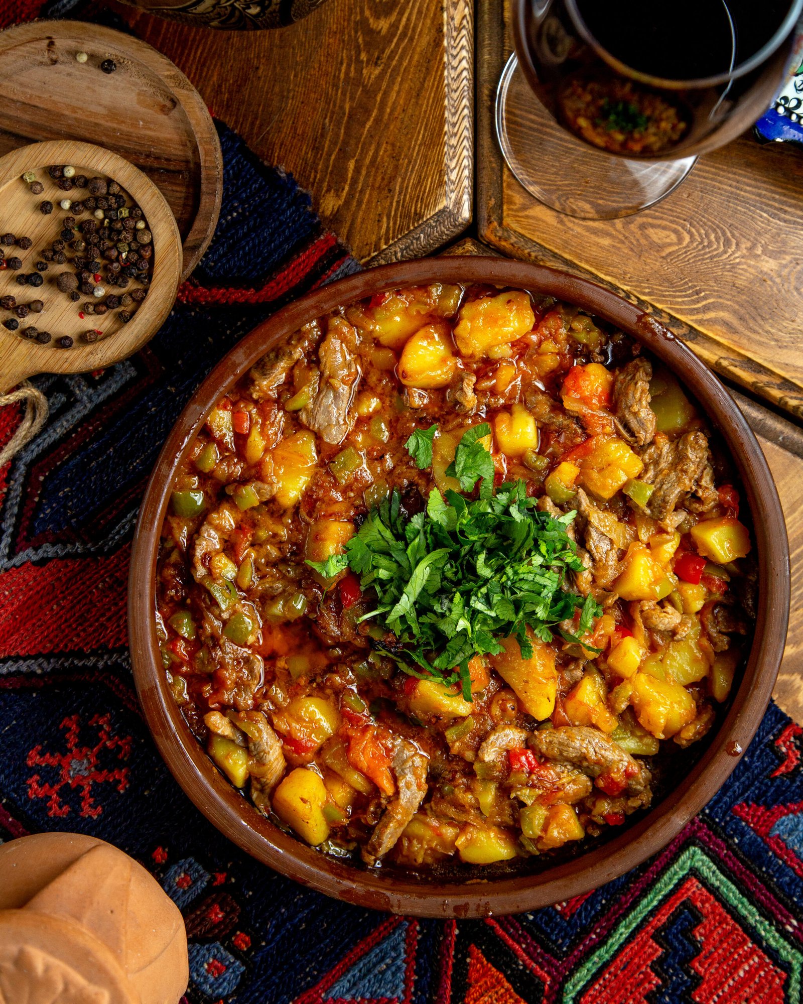 top view of stewed beef meat with potatoes green pappers and herbs in a clay bowl on a wooden table