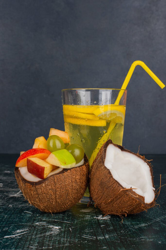 Various fruits in half cut coconut and glass of juice on marble table