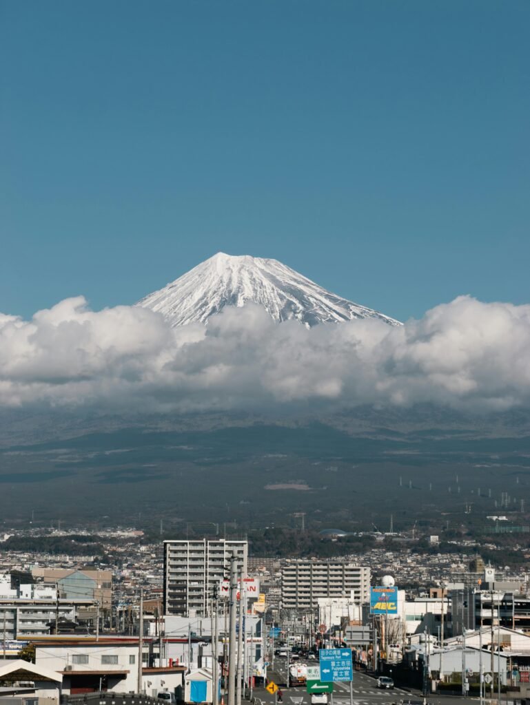 pexels-photo-19777821-19777821 A breathtaking view of snow-capped Mount Fuji towering over the city of Shizuoka in Japan, framed by clouds.