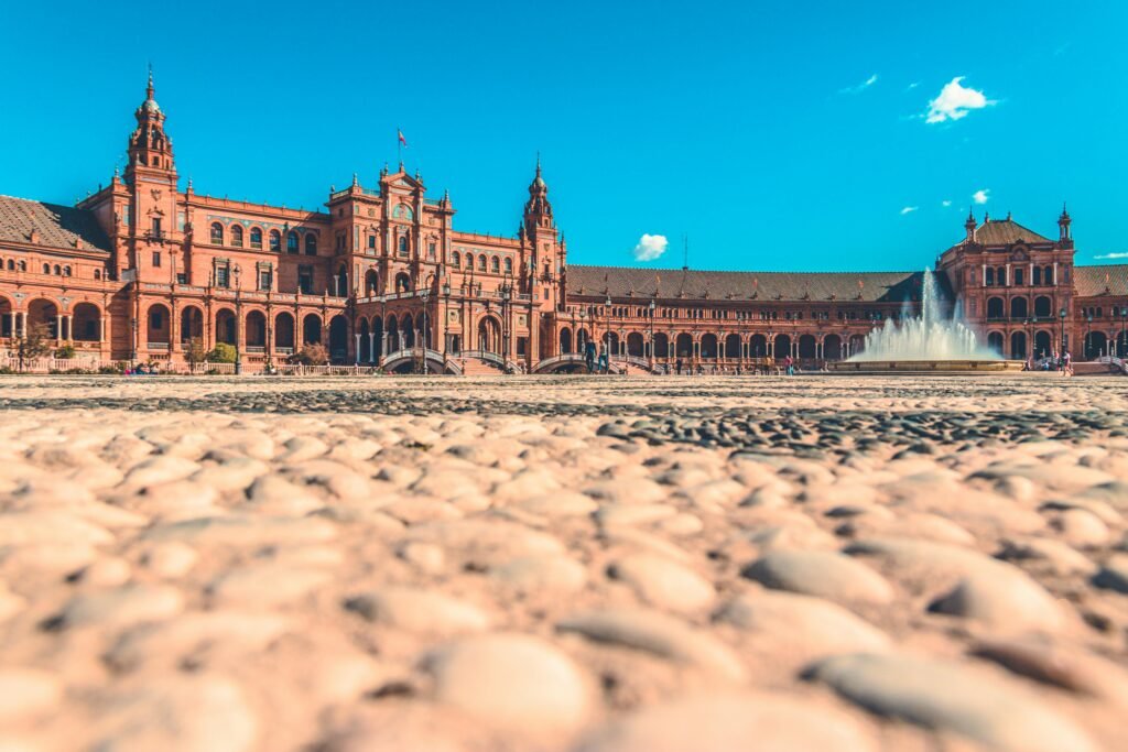 A scenic view of Plaza de España in Seville, Spain, featuring the iconic fountain and unique architecture under a clear blue sky.