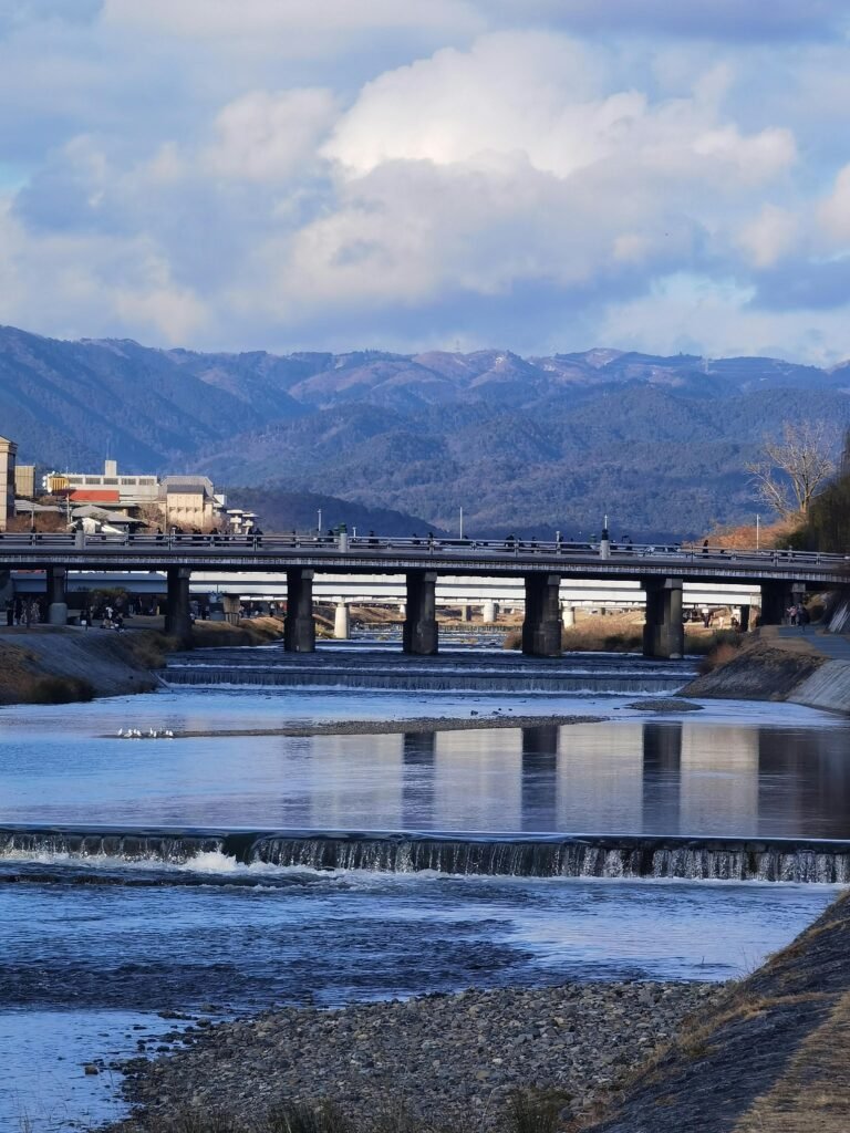 pexels-photo-31199090-31199090 Serene view of a river flowing under a bridge with distant mountains, capturing Kyoto's beauty.