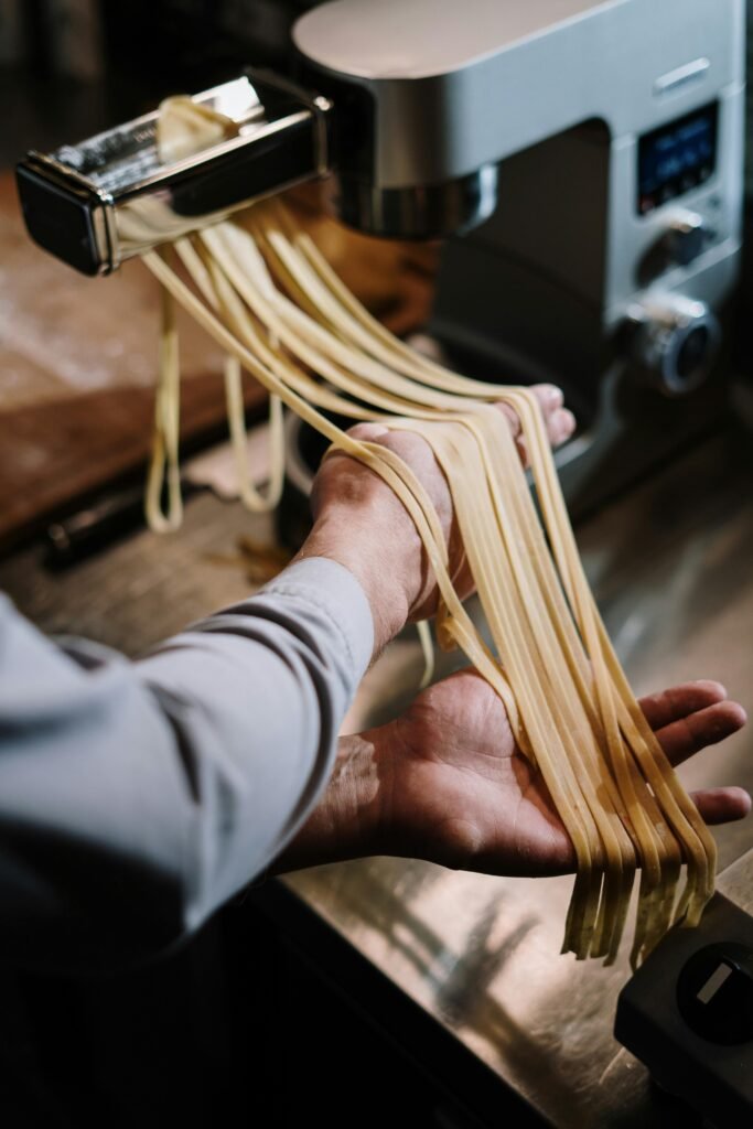 pexels-photo-4252770-4252770 Hands guiding fresh pasta through a pasta machine in a home kitchen setting.
